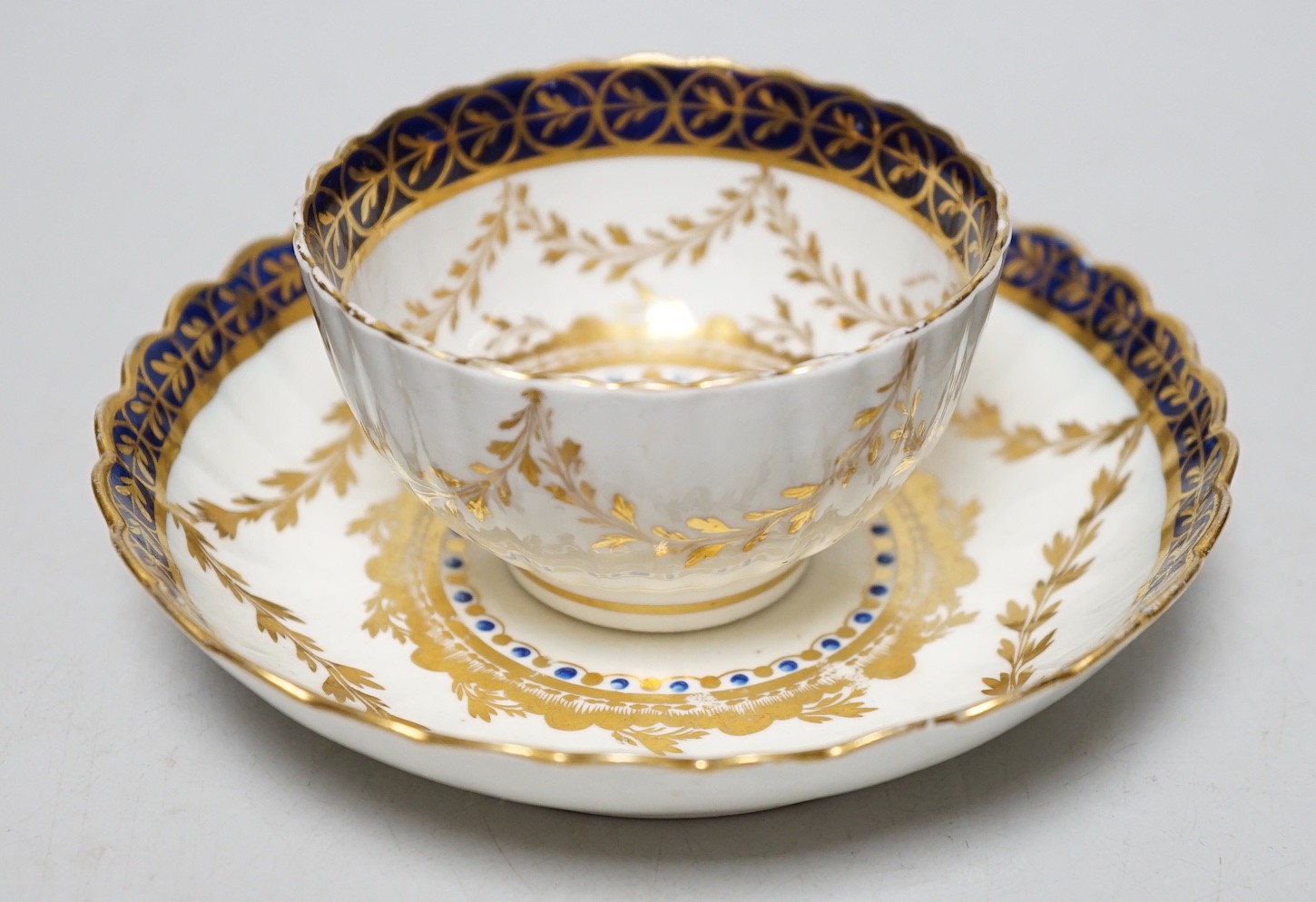 An 18th century Caughley rare teabowl and saucer painted with a crest of an arm clutching a dragon encircled by three gilt borders, 6cm tall overall